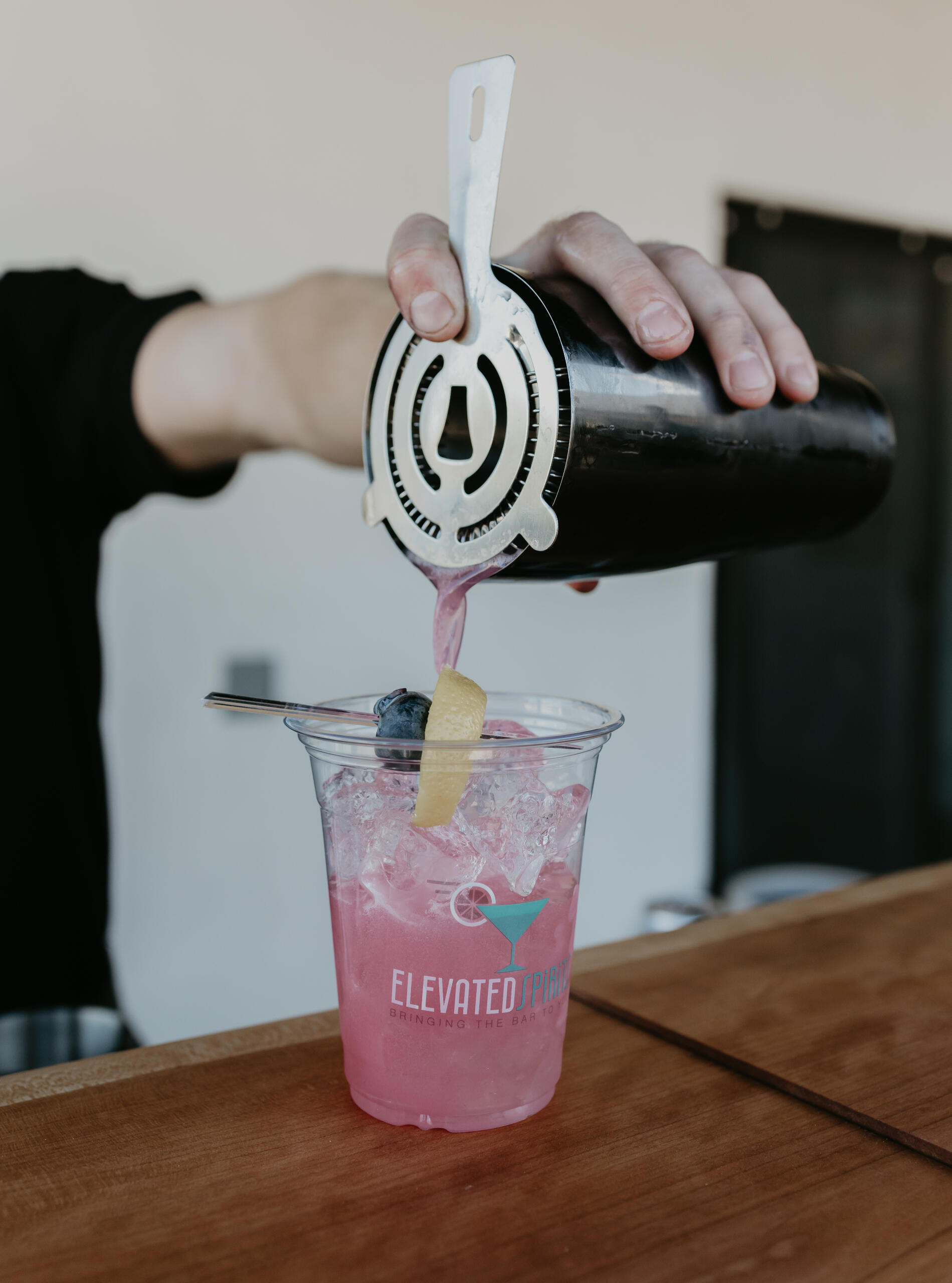Custom Cocktail Service Bartender straining a pink signature cocktail into a branded Elevated Spirits cup.