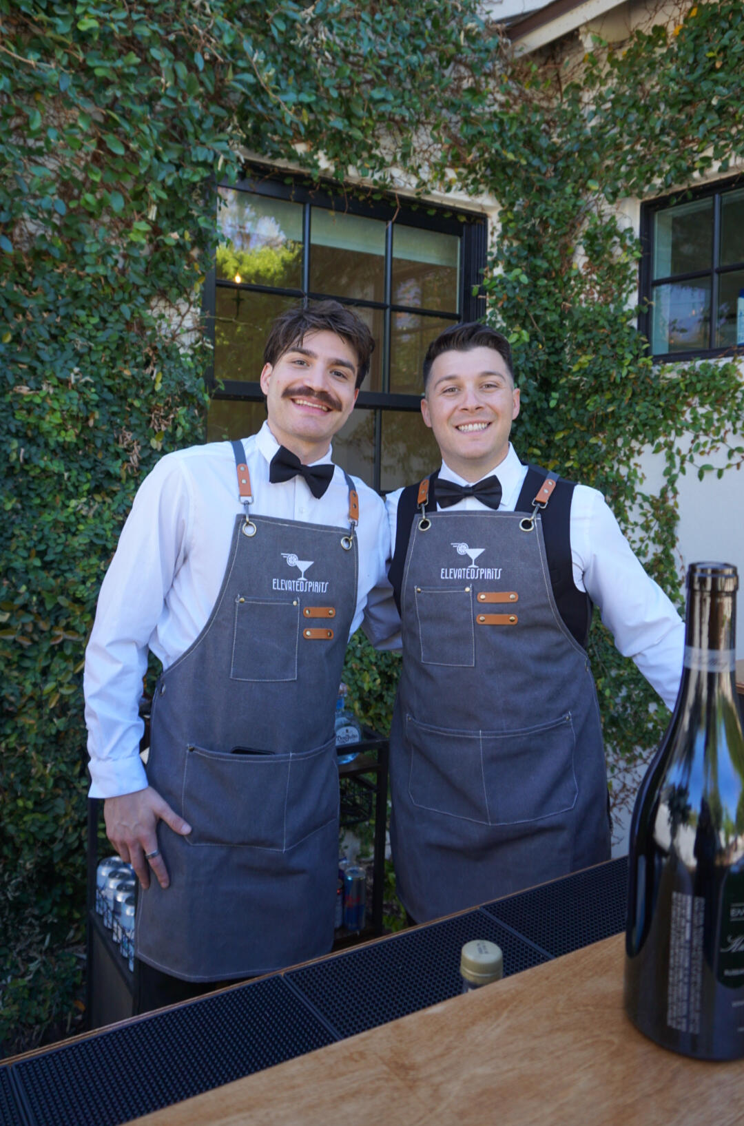 Elevated Spirits Professional Bartenders Two Elevated Spirits bartenders wearing branded aprons behind an event bar.