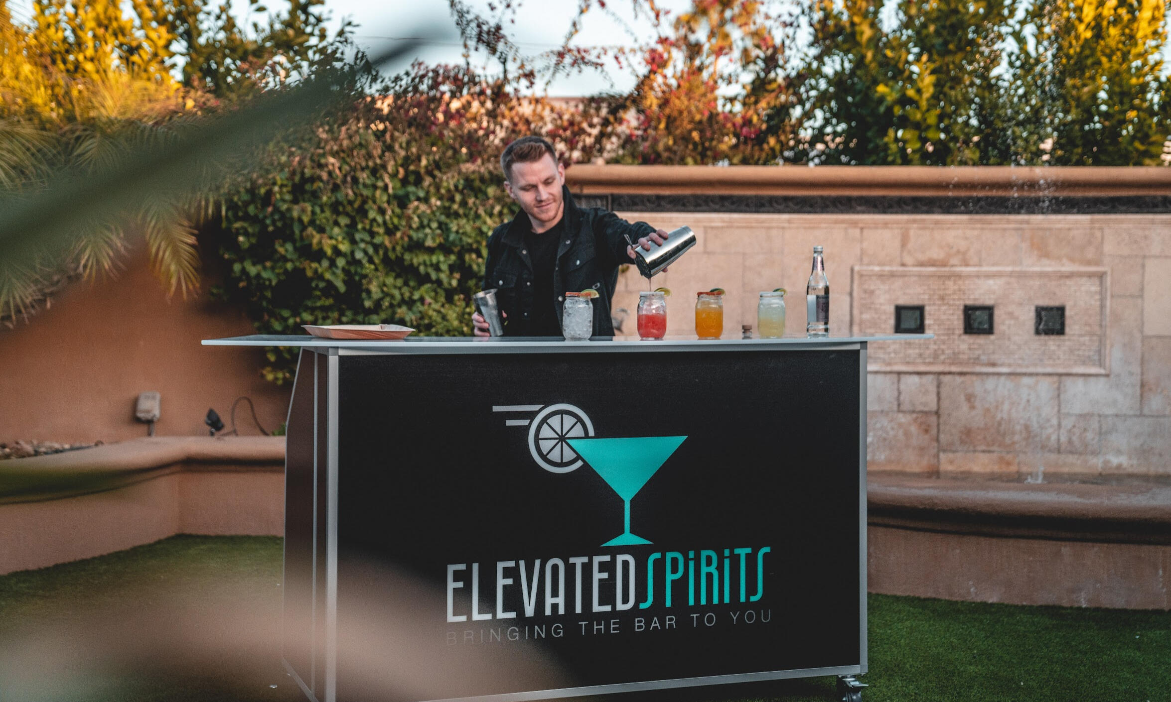 Bartender serving drinks behind an Elevated Spirits portable bar at an outdoor event.