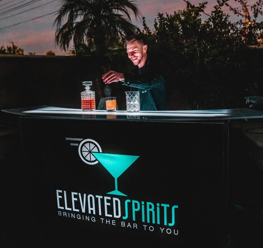 Bartender serving cocktails from an Elevated Spirits mobile bar at an outdoor event.