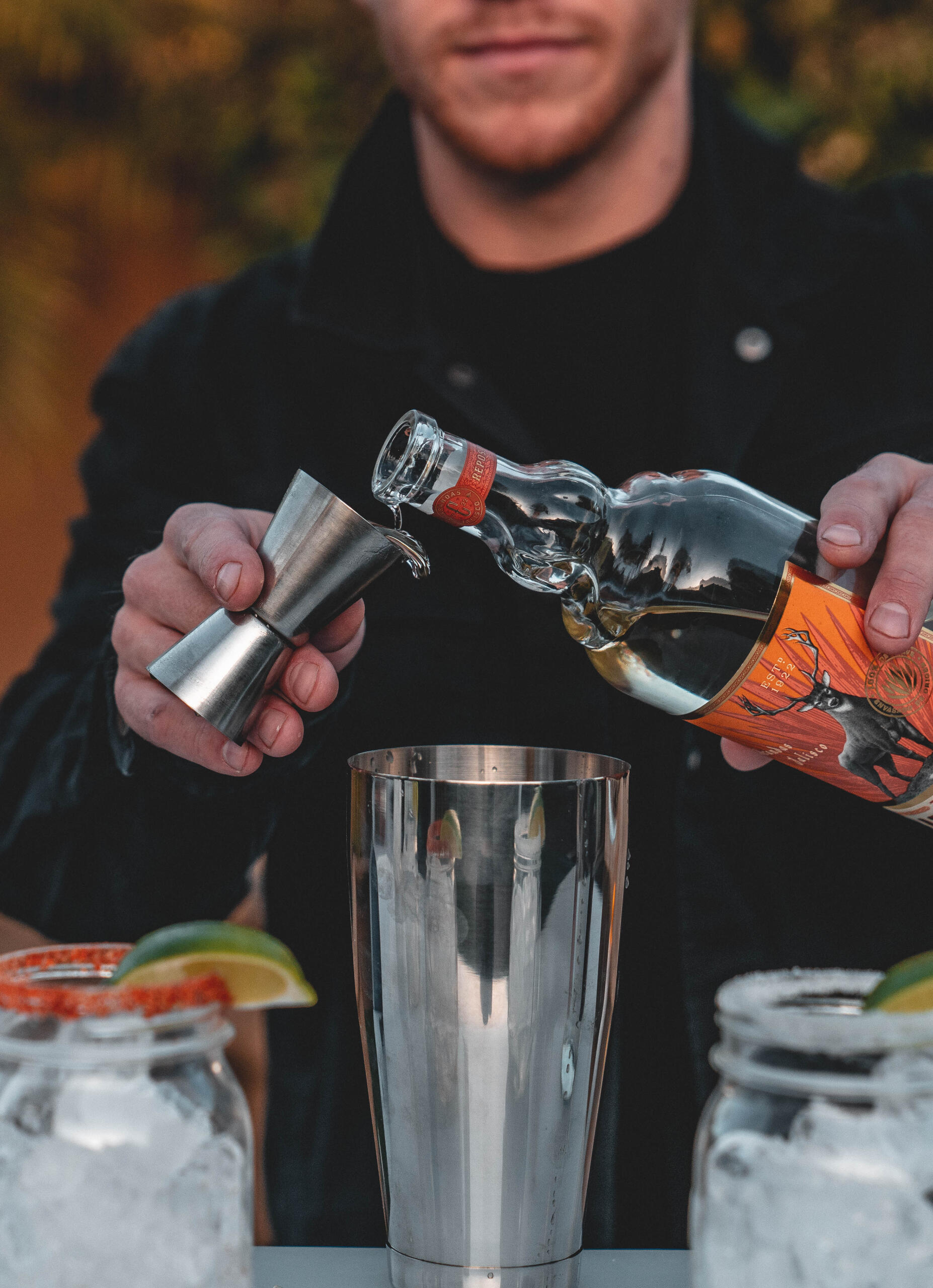 Professional Cocktail Bartending Bartender measuring spirits with a jigger while preparing cocktails at an event.